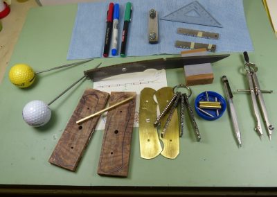 Knife blank on working bench with parts and tools
