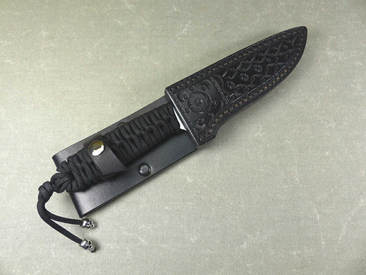 Black paracord camping knife inside matching black leather sheath