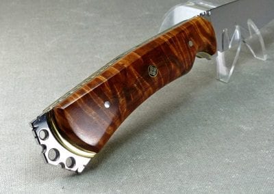Sculptured metal crown on end of brown flame maple knife handle showing exposed brass plate