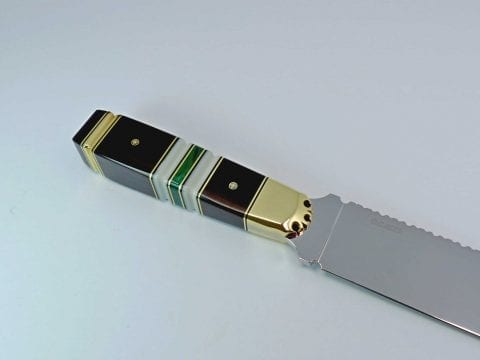 Brass embellishments at top and bottom of black knife handle with three bands of white and green stone in the middle