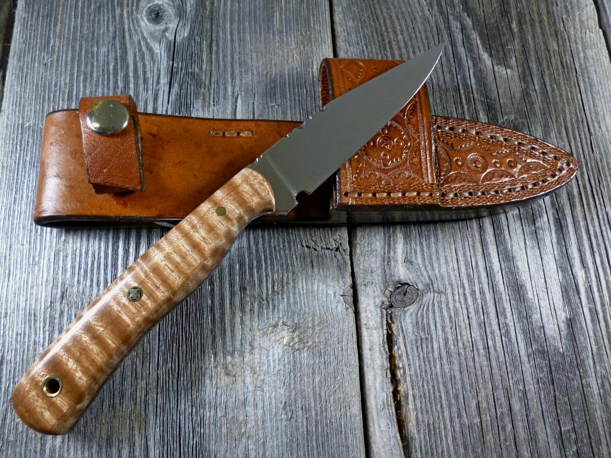 Knife with brown wood handle and sharp blade resting on top of brown hand tooled leather sheath