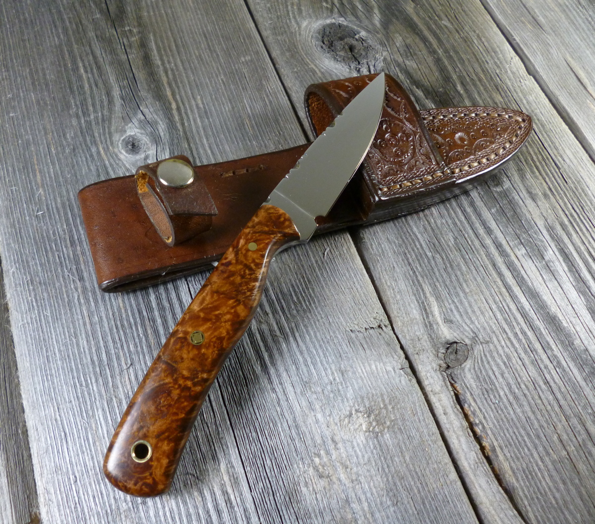 Handmade glossy dark brown clip point EDC knife resting on leather sheath on top of grey board