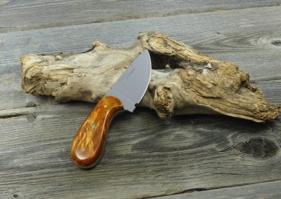 Small skinning knife made from figured maple resting on piece of wood