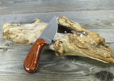 Small hunting knife made of stripped wood resting on driftwood